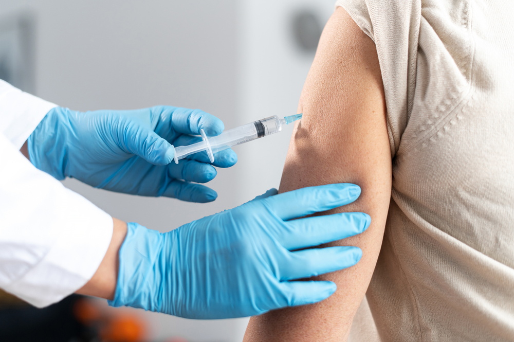 Un femeie cu mănuși de protecție, injectează o doză de vaccin unui pacient