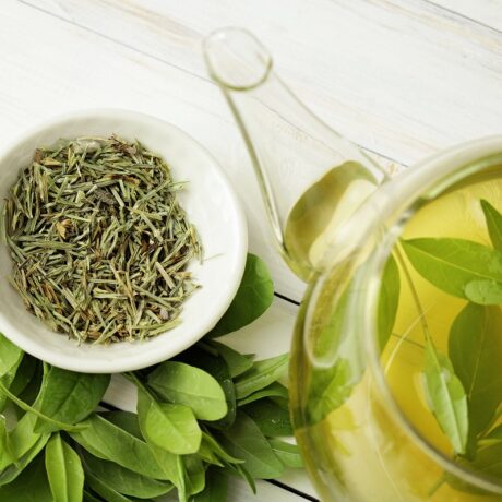 Ceașcă i ceainic cu ceai verde și frunze de ceai verde, unul dinre cele mai recomandate ceaiuri care scad trigliceridele