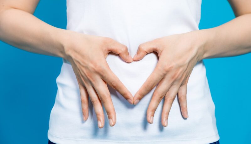 Femeie care formează o inimă cu mâinile pe adomen, sugestiv pentru o sarcină și când apar primele semne de sarcină