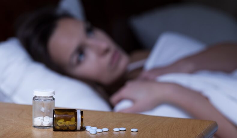 Femeie care stă în pat cu pastile pe noptieră