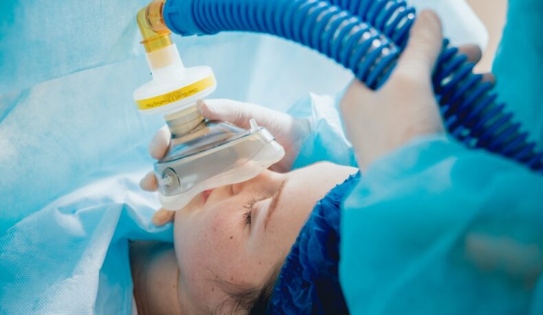 Femeie în spital care a primit anestezie totală și i se pune mască de oxigen, sugestiv pentru efectele adverse ale anesteziei