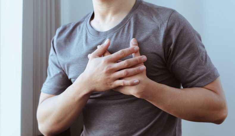 Bărbat care se ține cu mâinile de piept, sugestiv pentru durerea în piept, nul dintre cele mai comune semne care prevestesc infarctul
