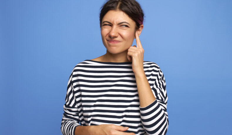 O femeie tânără își duce degetul la ureche din cauza unui simptom neplăcut