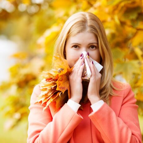 Femeie care își suflă nasul în peisaj de toamnă, sugestiv pentru răceli și alergii - cele mai comune boli ale toamnei