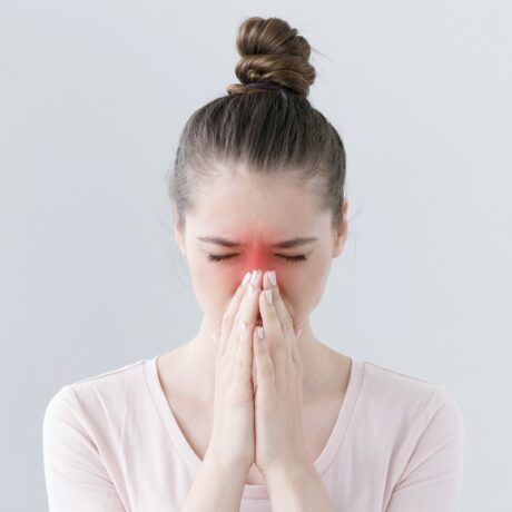 Femeie cu durere de sinuzită care ține mâinile la nas