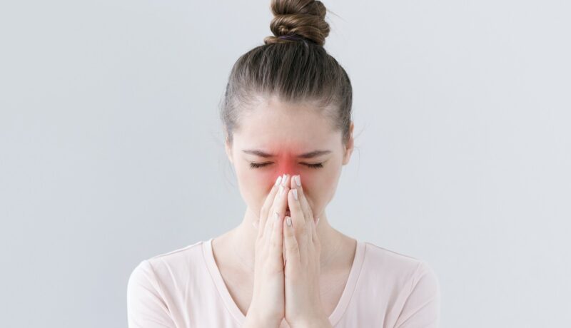 Femeie cu durere de sinuzită care ține mâinile la nas
