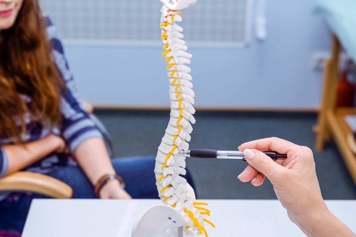 Pacientă și medic care arată către o machetă a coloanei vertebrale, sugestiv pentru osteoporoza la femei