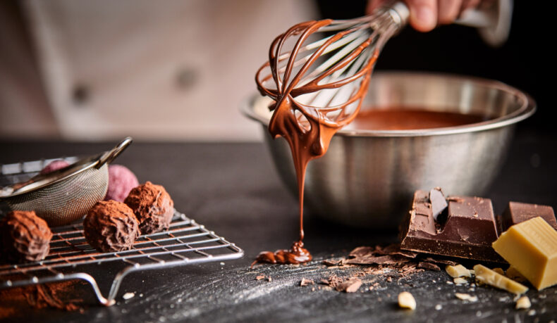 Un bărbat prepară ciocolată cu ajutorul mai multor ustensile, amestecate cu mai multe tipuri de ciocolată