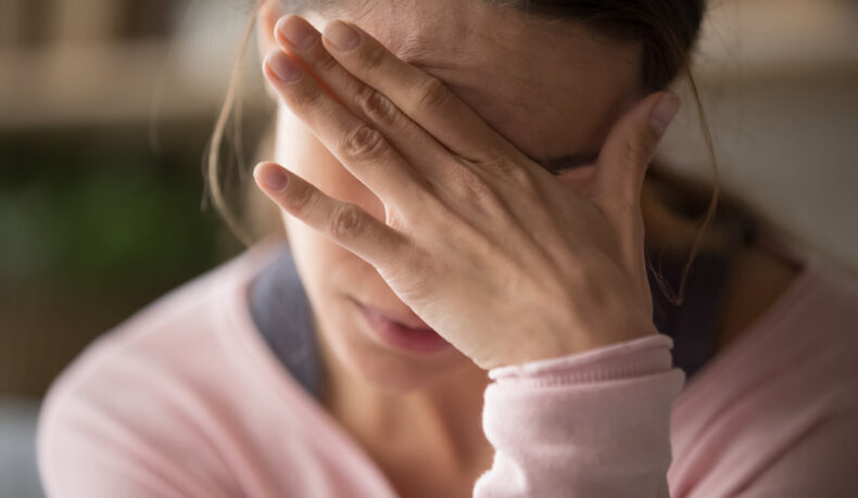 O femeie tânără își ține o mână pe față din cauza unei dureri