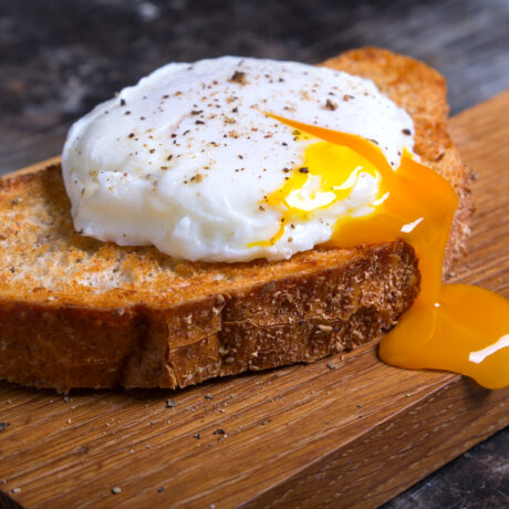 Un ou poșat pe pâine prăjită, pe un tocător din lemn