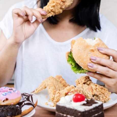 O femeie tânără care consumă mâncare fast food și multe dulciuri