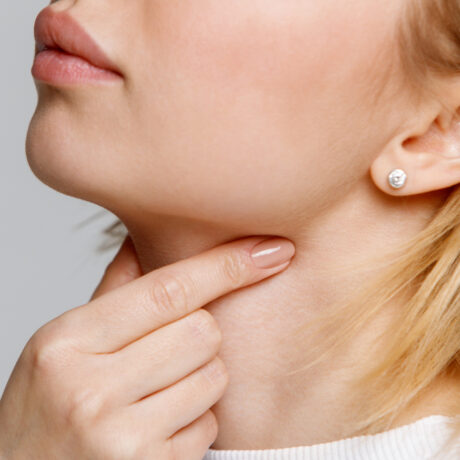 O femeie tânără își atinge gâtul din cauza durerilor