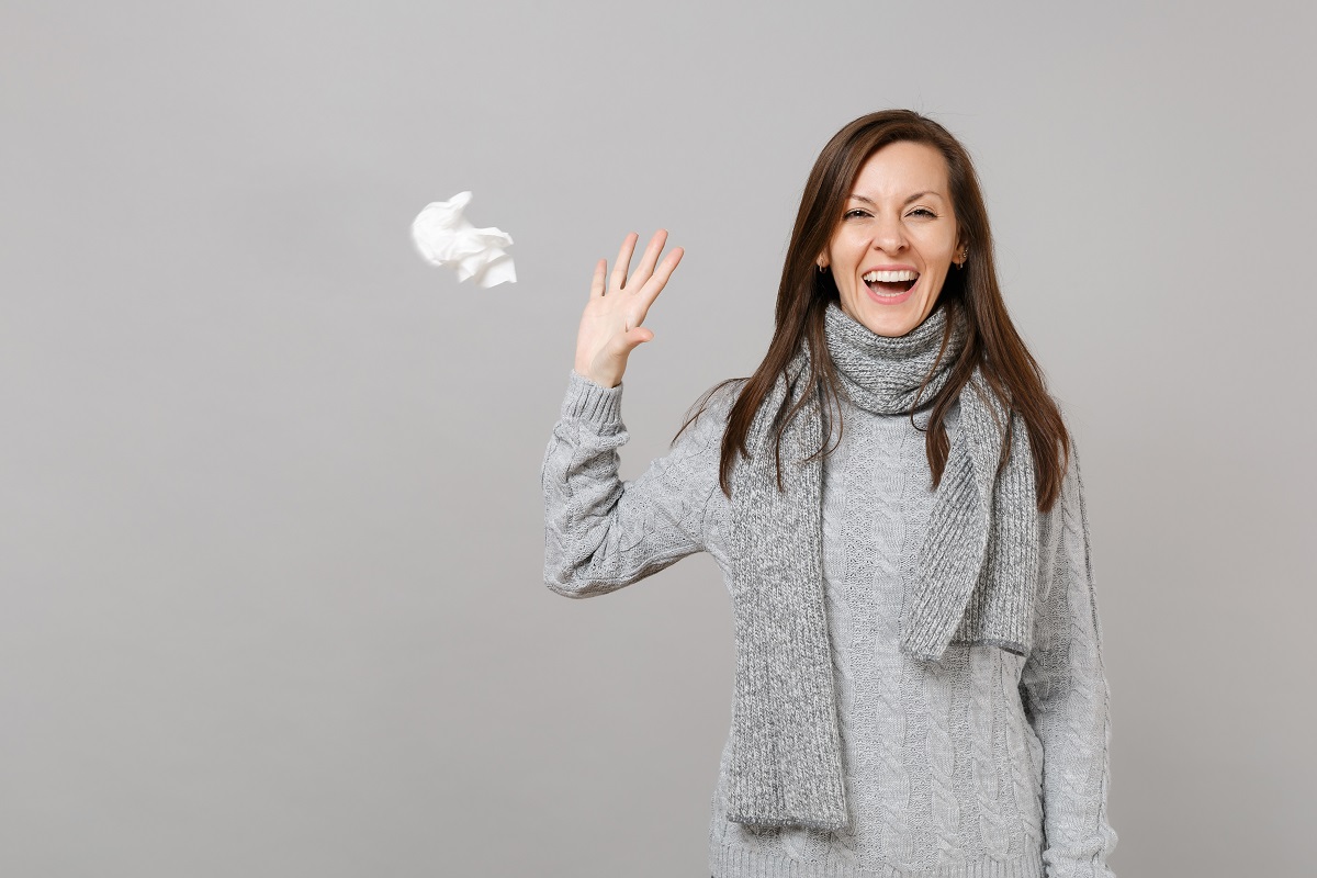 Femeie care râde și aruncă un șervețel, sugestiv pentru Cum poți preveni răceala și gripa