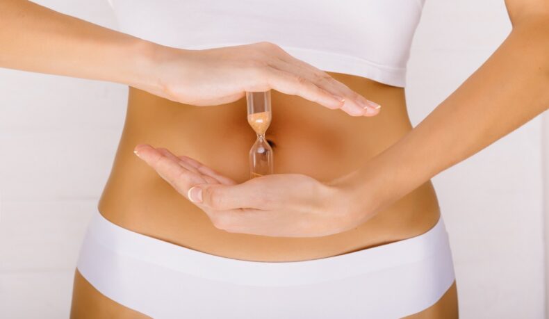 Femeie care ține o clepsidră în dreptul abdomenului, sugestiv pentru timpul de digestie a alimentelor