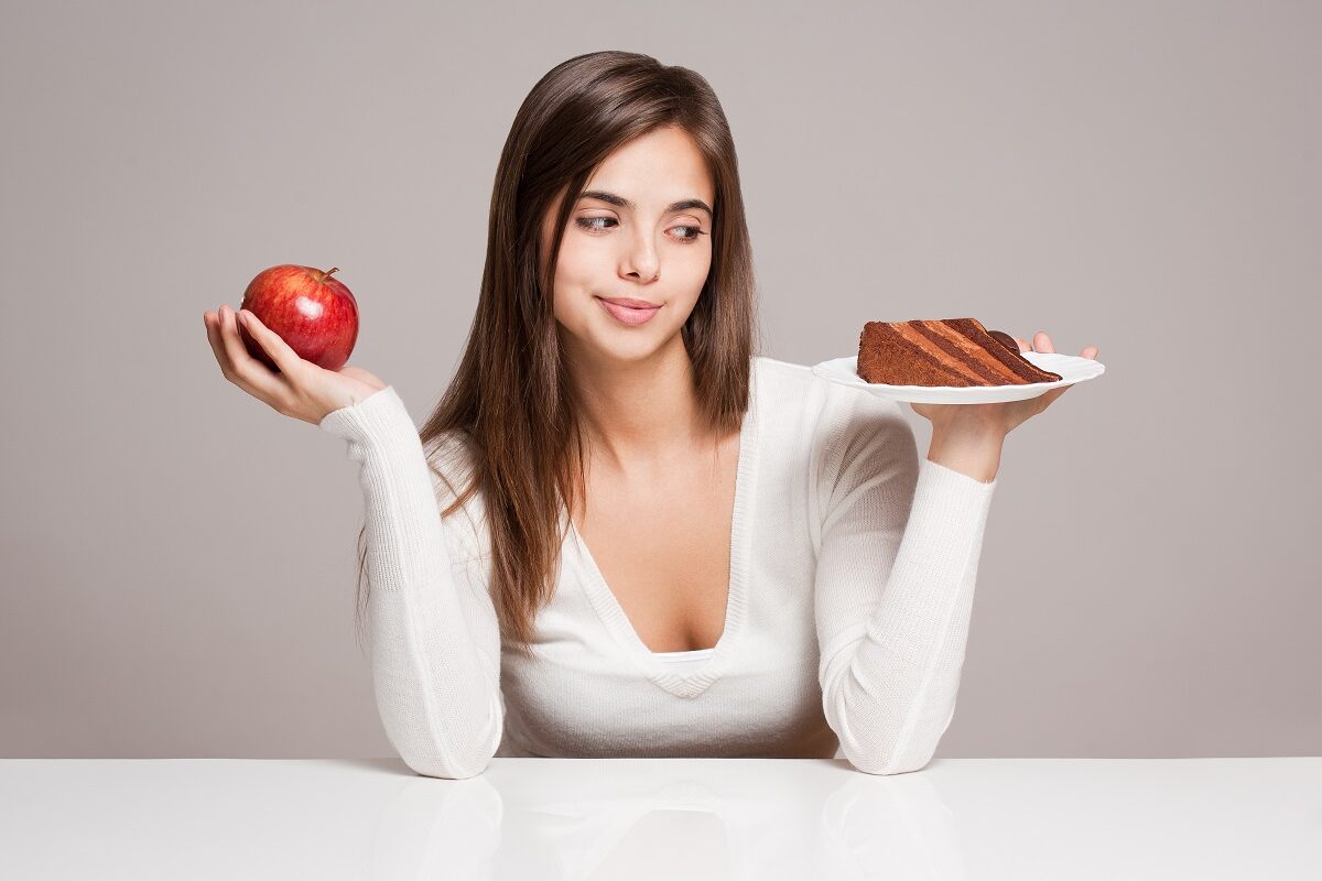 Femeie cu un măr și o femie de tort în mâini, sugestiv pentru trucuri care te scapă de pofta de dulce