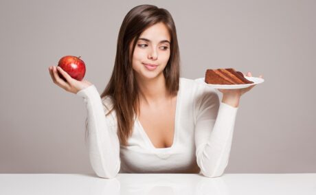 Femeie cu un măr și o femie de tort în mâini, sugestiv pentru trucuri care te scapă de pofta de dulce