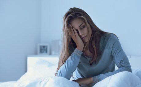 Femeie obosită care stă în pat, sugestiv pentru lipsa de somn