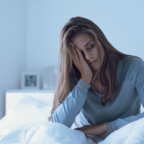 Femeie obosită care stă în pat, sugestiv pentru lipsa de somn