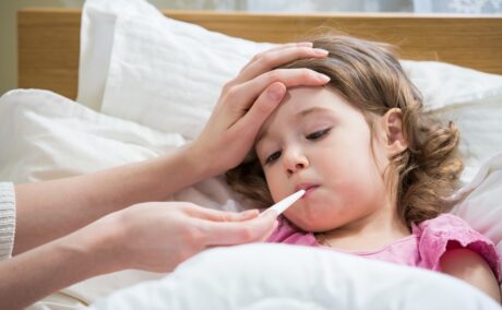 Fetiță bolnavă cu febră și cu termometru în gură, febra fiind unul dintre simptomele infecției cu virusul sincițial respirator