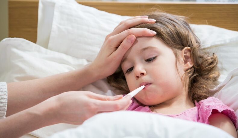 Fetiță bolnavă cu febră și cu termometru în gură, febra fiind unul dintre simptomele infecției cu virusul sincițial respirator
