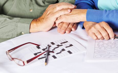 Vârstnici care se țin de mâini și un rebus nerezolvat pe masă, sugestiv pentru Alzheimer sau alte tipuri de demență