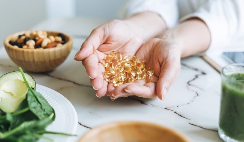 Un nutriționist ține în mâini capsule cu vitamine, la o masă cu alimente naturale