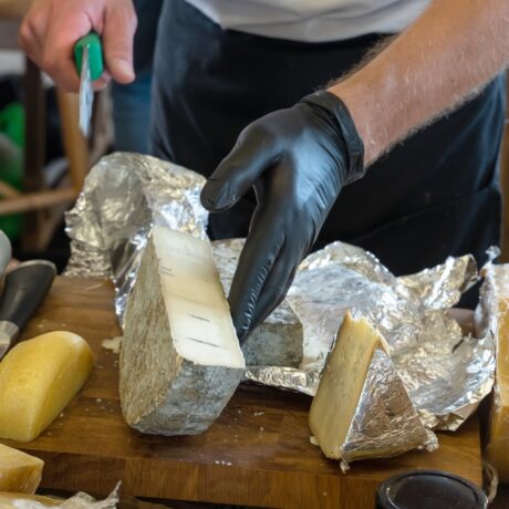 Un bărbat tânăr care poartă mănuși taie mai multe tipuri de brânză într-un decor cu mai multe folii