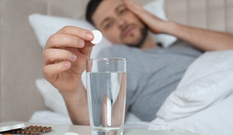 Bărbat cu durere de cap care pune o pastilă într-un pahar cu apă, sugestiv pentru remedii rapide pentru mahmureală