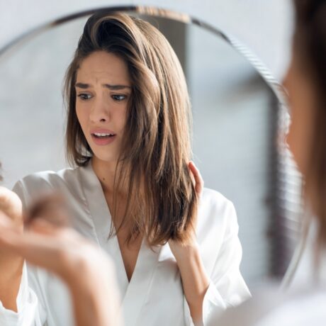 O femeie tânără ține îngrijorată în fața oglinzii, câteva fire de păr