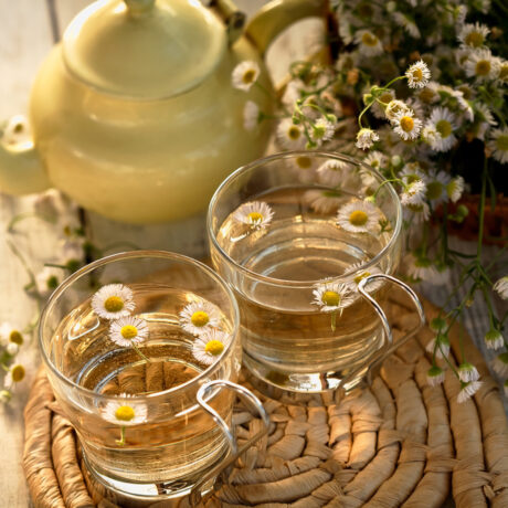 Două căni cu ceai, alături de un ceainic și flori de mușețel