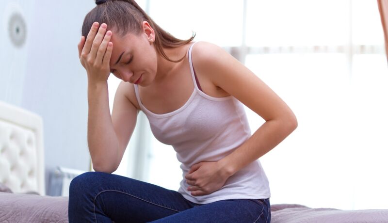 Femeie cu durere de burtă și de cap, simptome sugestive pentru sindromul premenstrual