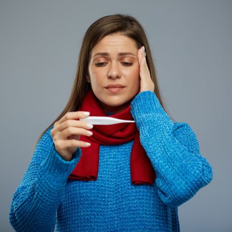 Femeie cu durere de cap care se uită la un termometru