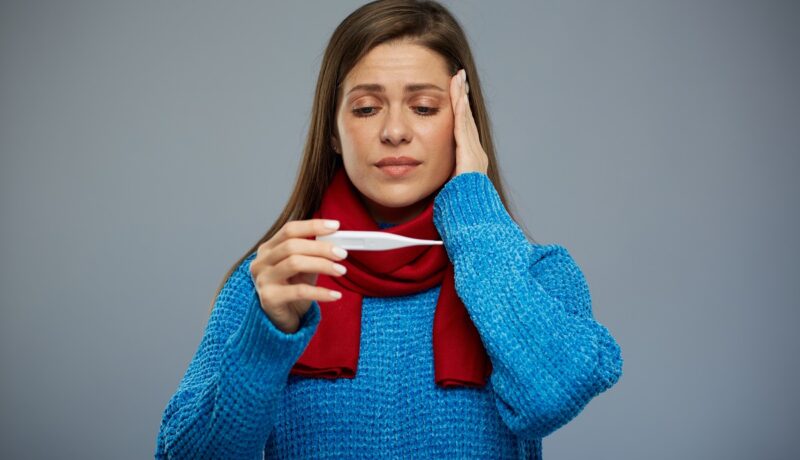 Femeie cu durere de cap care se uită la un termometru