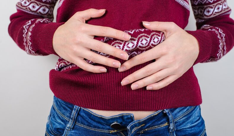 Femeie cu mâinile pe burtă și nasture desfcut la pantaloni, sugestiv pentru ce să faci dacă ai mâncat prea mult