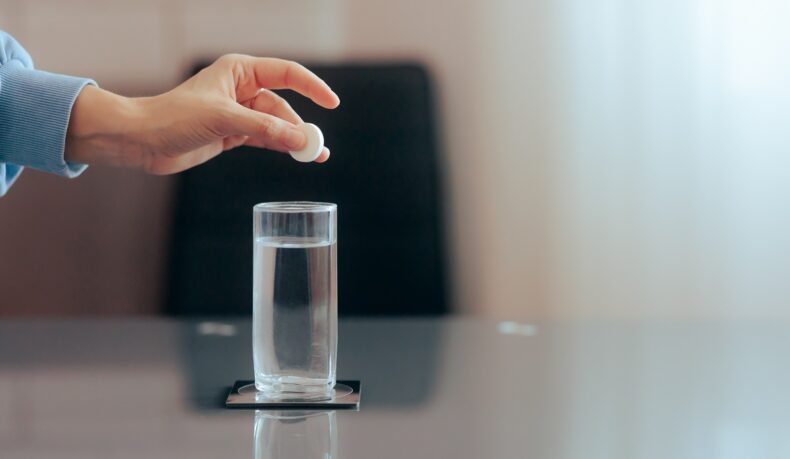 Detaliu cu mână care pune o pastilă efervescentă într-un pahar cu apă, care poate fi un supliment cu magneziu pentru anxietate