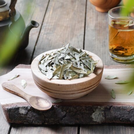 Un vas din lemn cu frunze de senna, lângă un ceainic și un pahar cu ceai