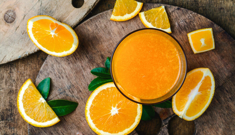 Un bol cu suc de portocale, înconjurat de bucăți de portocale