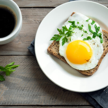 O felie cu un ou prăjit, pe o farfurie, lângă: o ceașcă cu cafea, o solniță și o furculiță pe un șervet