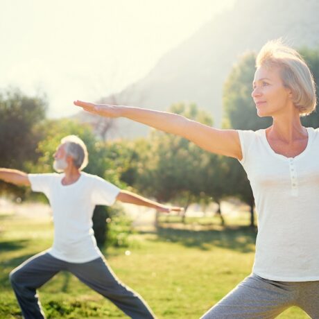 Cuplu de vârstnici care face yoga în parc, sugestiv pentru un stil de viață sănătos