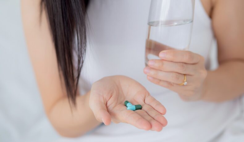 Femeie cu două antibiotice în palmă și un pahar cu apă, sugestiv pentru candidoza de la antibiotice
