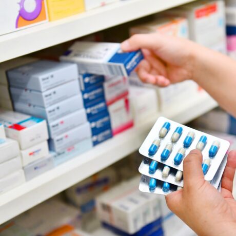 farmacist cu o cutie de antibiotice în mână, la raftul din farmacie