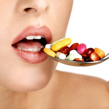 Femeie care ia o lingură de pastile colorate, sugestiv pentru riscurile suplimentelor alimentare