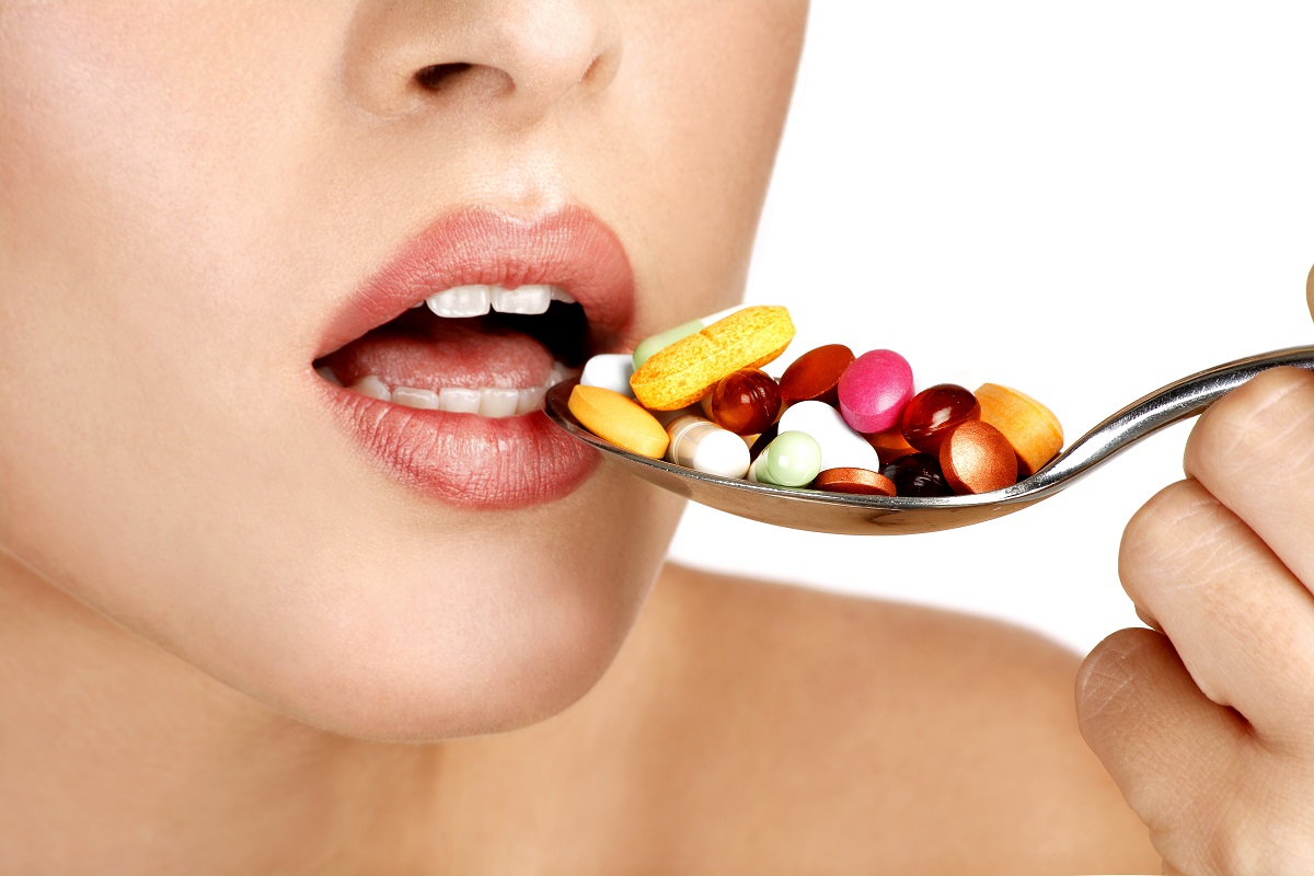 Femeie care ia o lingură de pastile colorate, sugestiv pentru riscurile suplimentelor alimentare