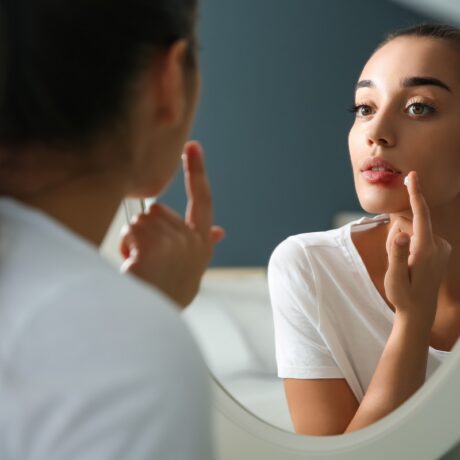 Femeie care se uită în oglindă și aplică o cremă pe herpesul bucal