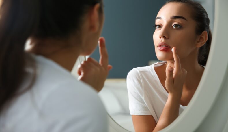 Femeie care se uită în oglindă și aplică o cremă pe herpesul bucal