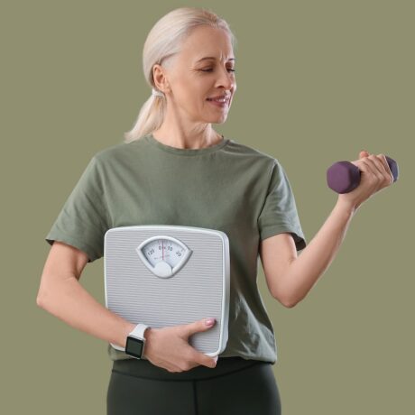 Femeie în vârstă cu cântar în brațe și ganteră în mână, sugestiv pentru accelerarea metabolismului