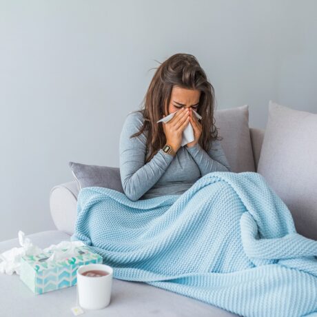 Femeie răcită care stă pe canapea și își suflă nasul