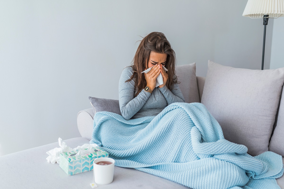 Femeie răcită care stă pe canapea și își suflă nasul