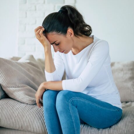 Femeie tristă, deprimată pe canapea, depresia fiind unul dintre primele simptome de scleroză multiplă