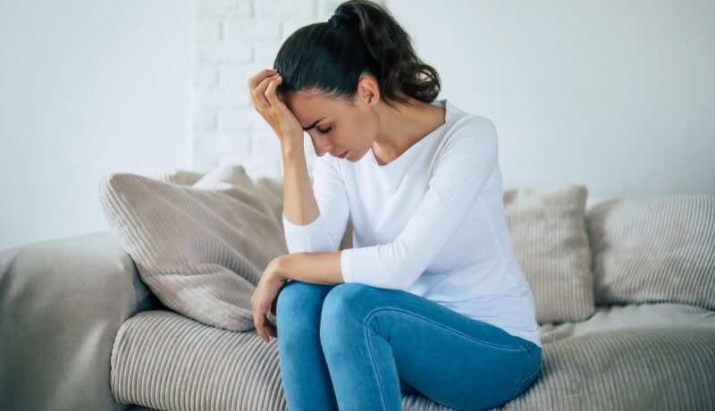 Femeie tristă, deprimată pe canapea, depresia fiind unul dintre primele simptome de scleroză multiplă